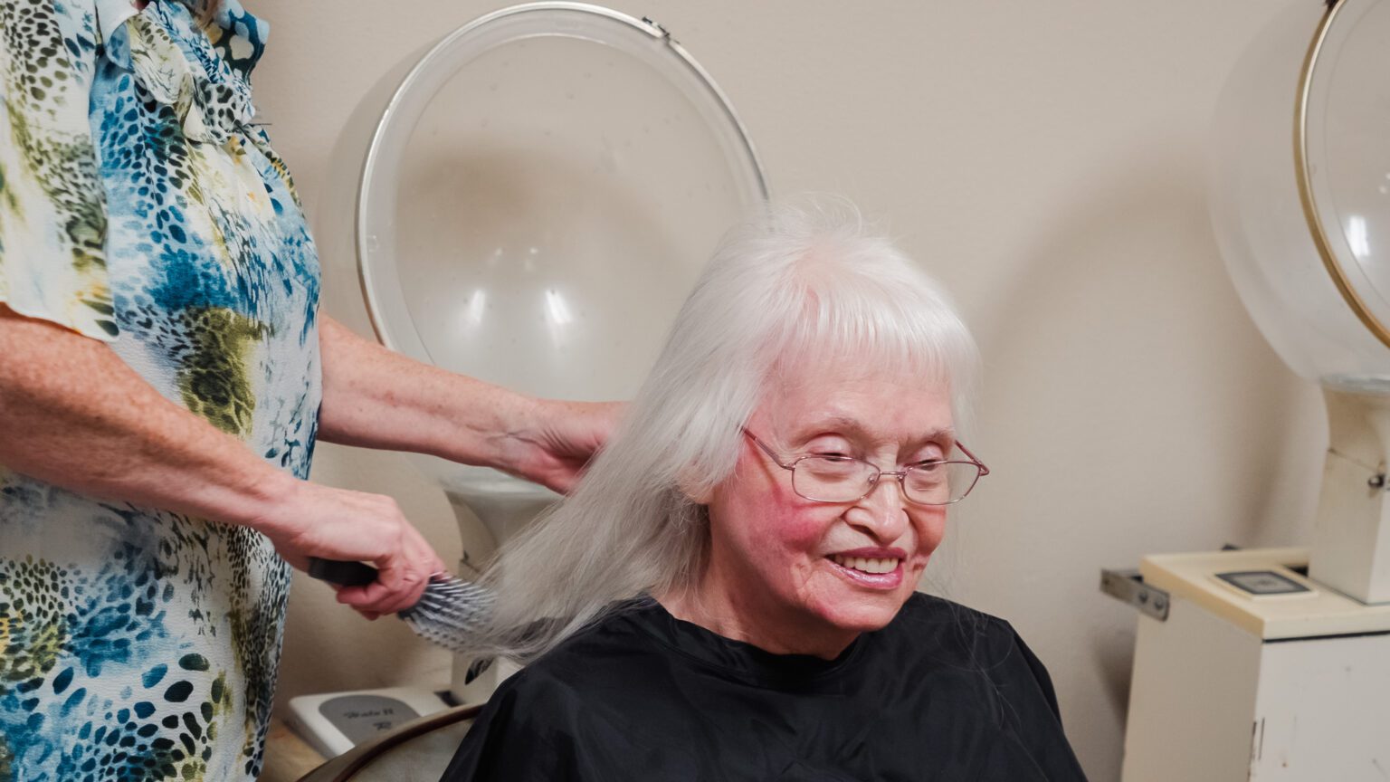 A woman getting her hair done by a stylist at a skilled nursing facility nursing home