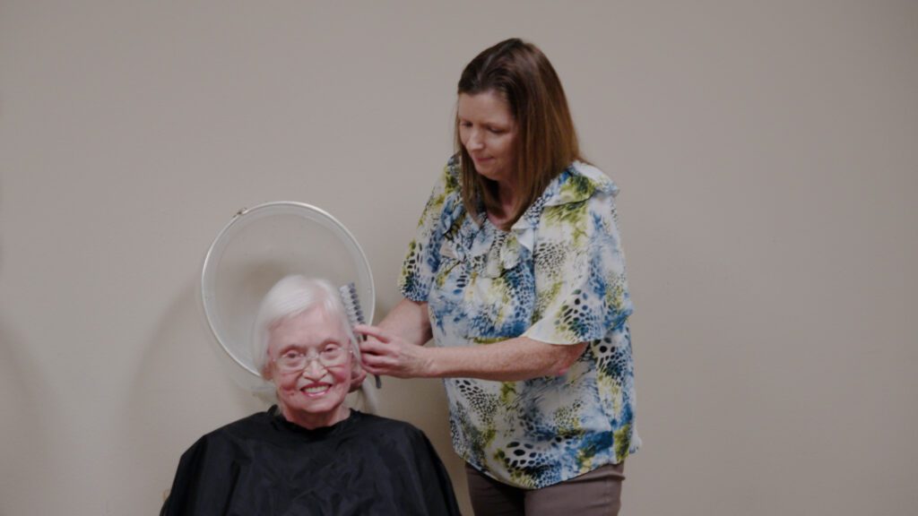 A woman getting her hair done by a stylist at a skilled nursing facility nursing home